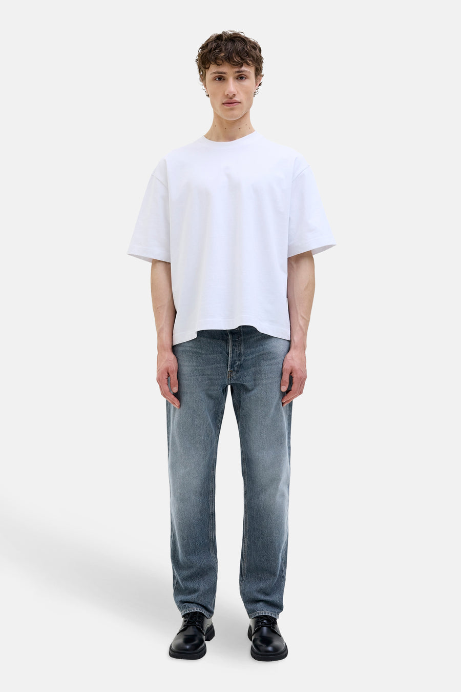 Jean fuselé en denim bleu moyen de JACK & JONES JEANS INTELLIGENCE, porté avec un t-shirt blanc et des chaussures noires.
