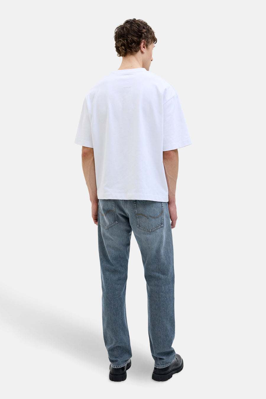 Jean fuselé bleu moyen en denim de JACK & JONES JEANS INTELLIGENCE, porté avec un t-shirt blanc et des chaussures noires, vue de dos.
