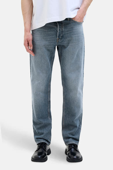 Jean fuselé en denim bleu moyen par JACK & JONES JEANS INTELLIGENCE, porté avec un t-shirt blanc et des chaussures noires.