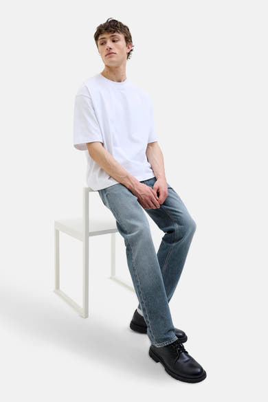 Jean fuselé bleu denim van JACK & JONES JEANS INTELLIGENCE, porté avec un t-shirt blanc et des chaussures noires.