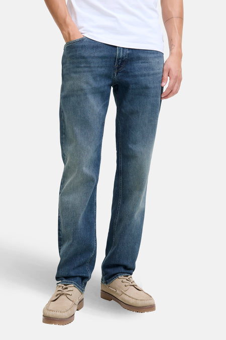 Jean droit en denim bleu moyen de JACK & JONES JEANS INTELLIGENCE, porté avec un t-shirt blanc et des chaussures bateau en daim beige.