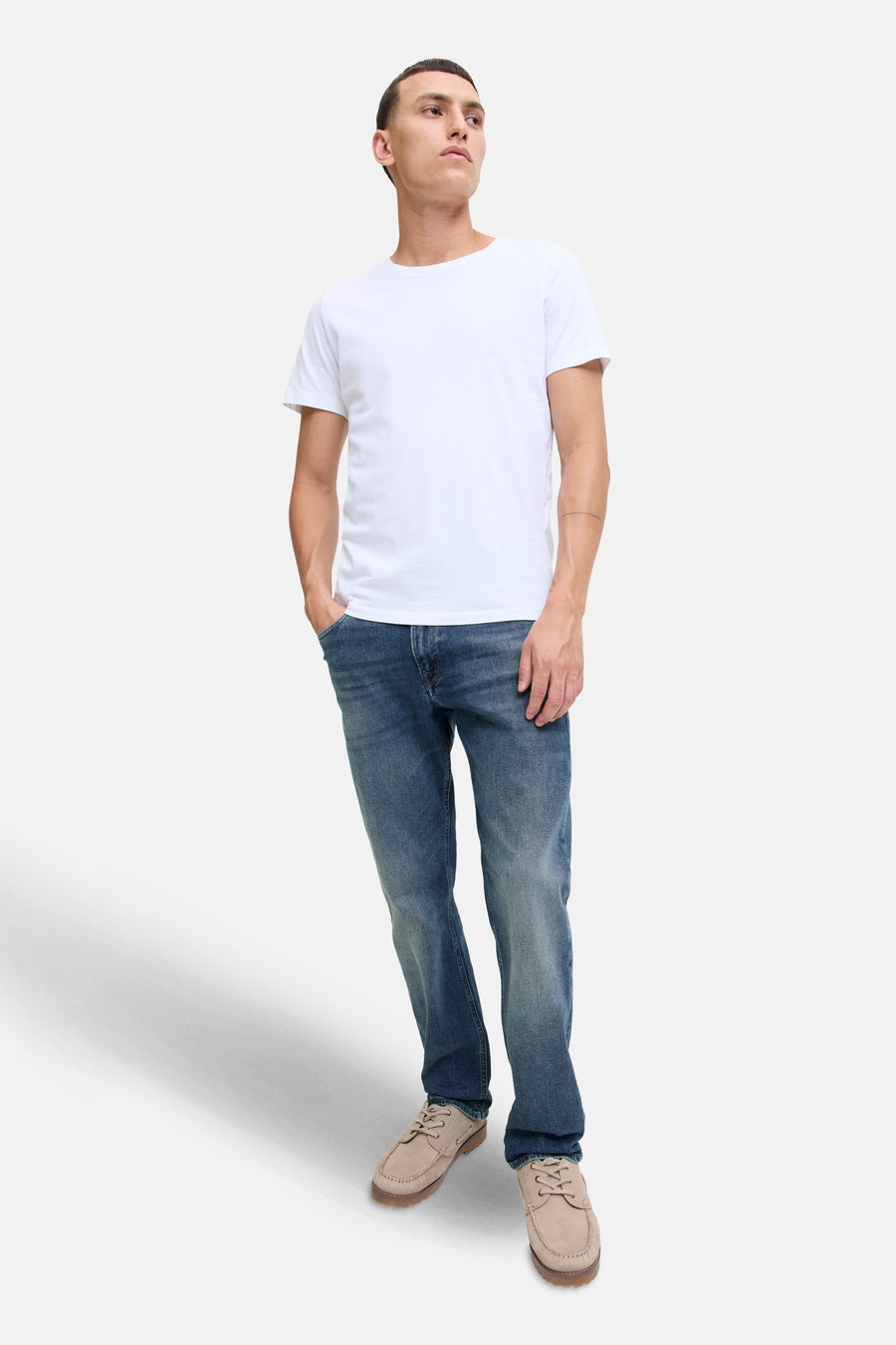 Rechte spijkerbroek in middinblauw denim van JACK & JONES JEANS INTELLIGENCE, gedragen met een wit T-shirt en beige suède bootschoenen.