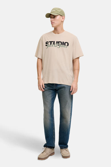 T-shirt à manches courtes écru de ORIGINALS BY JACK & JONES avec imprimé sur le devant, porté avec casquette et jean bleu.
