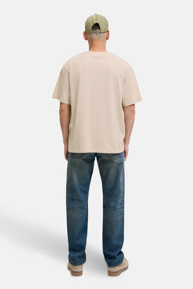 T-shirt à manches courtes écru de ORIGINALS BY JACK & JONES, porté avec un jean bleu et une casquette kaki.