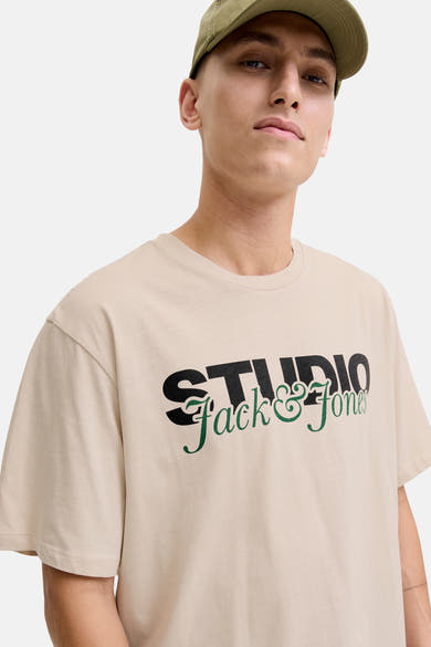 T-shirt à manches courtes écru d'ORIGINALS BY JACK & JONES avec un logo imprimé sur le devant et porté avec une casquette verte.