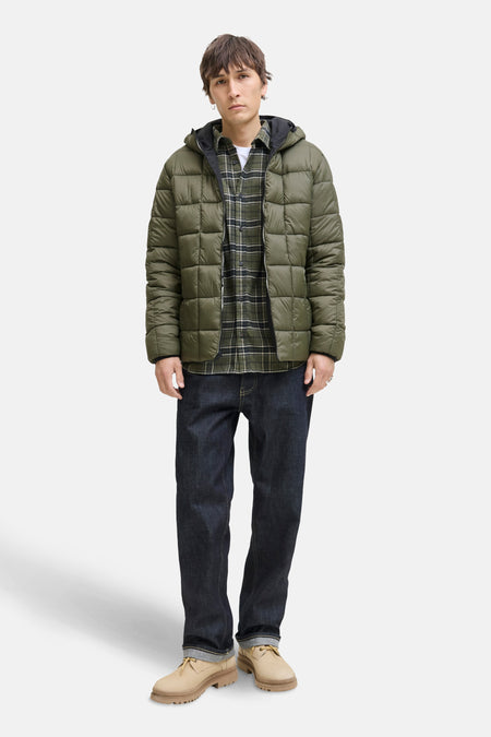 Zwarte regenjas van JACK & JONES met een gewatteerd pufferjack-ontwerp, gedragen over een geruit overhemd en een donkere spijkerbroek.