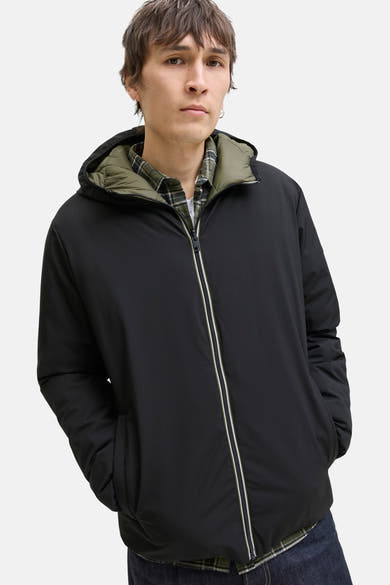 Zwarte regenjas van JACK & JONES, met capuchon en ritssluiting aan de voorkant, gedragen over een geruit overhemd.