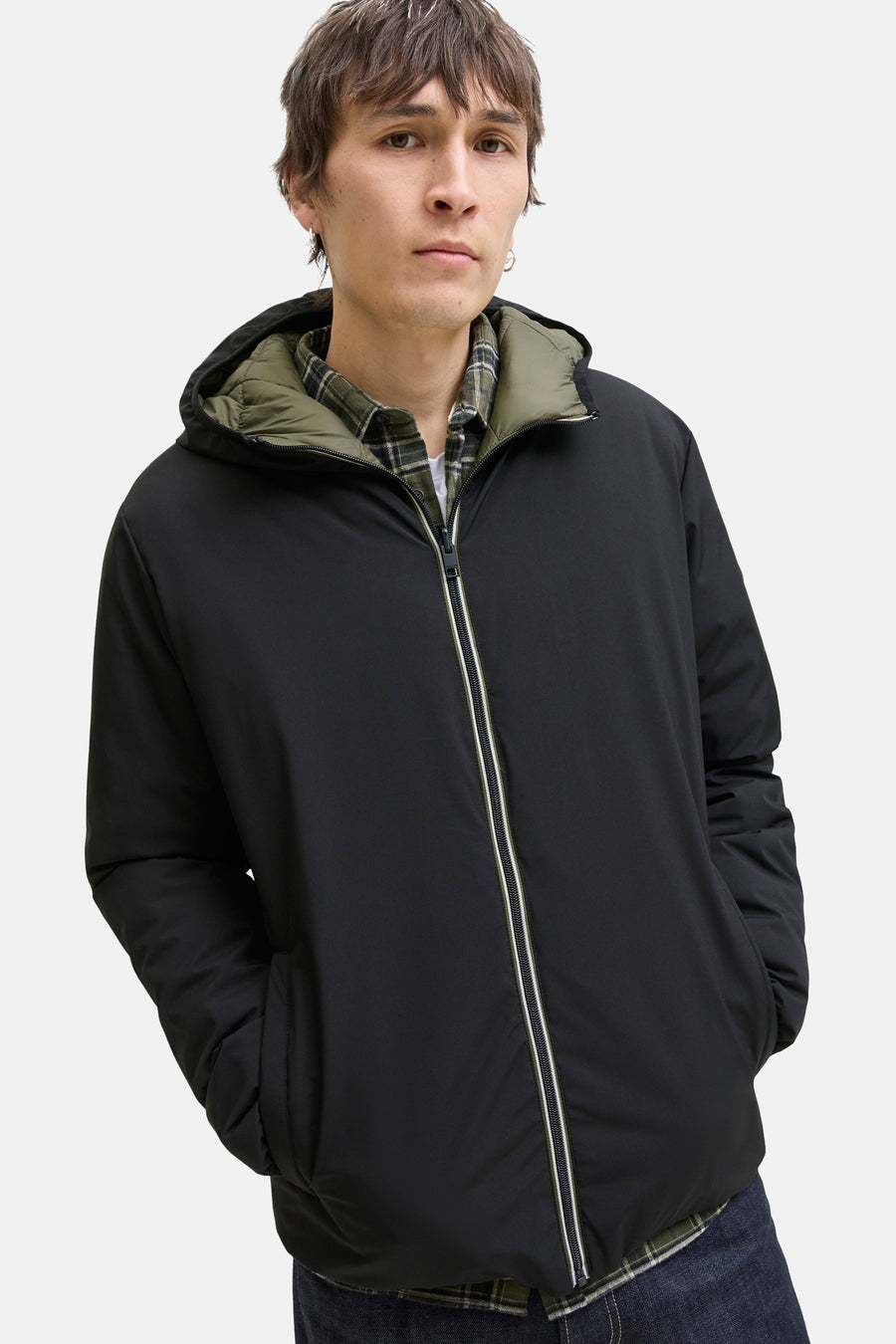 Zwarte regenjas van JACK & JONES, met capuchon en ritssluiting aan de voorkant, gedragen over een geruit overhemd.