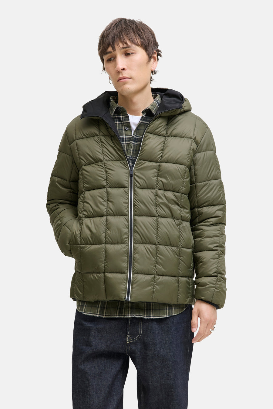 Zwarte regenjas van JACK & JONES met capuchon, gedragen over een geruit overhemd en een spijkerbroek.