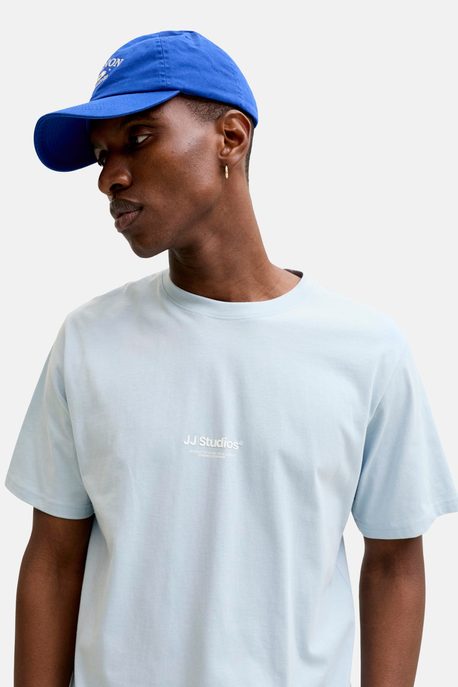T-shirt bleu à manches courtes de JACK & JONES, porté avec une casquette bleue et une boucle d'oreille dorée.