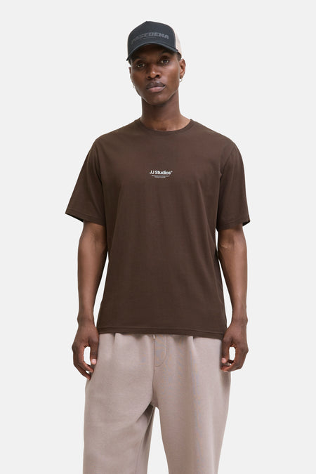 Bruin T-shirt met korte mouwen van JACK & JONES, gedragen met een beige joggingbroek en een pet.