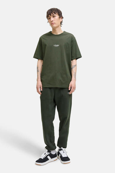 T-shirt à manches courtes vert de JACK & JONES, porté avec un pantalon de survêtement et des baskets.