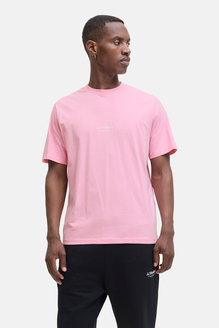 Roze T-shirt met korte mouwen van JACK & JONES, gedragen met een zwarte joggingbroek en zwart-witte sneakers.