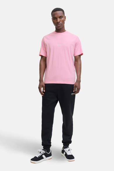 T-shirt à manches courtes rose de JACK & JONES, porté avec un pantalon de survêtement noir et des baskets noires et blanches.