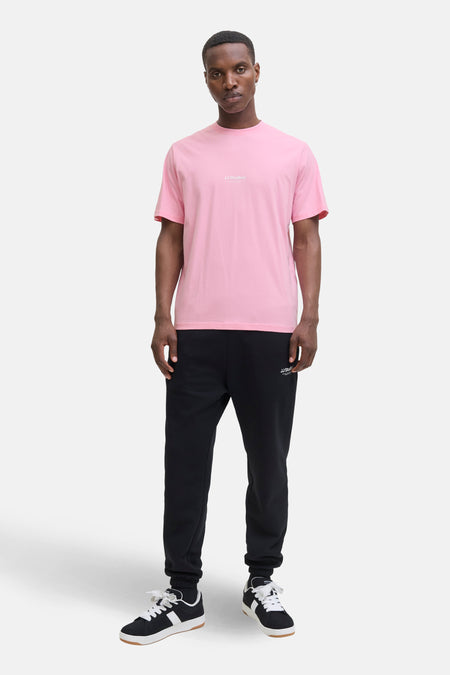 T-shirt à manches courtes rose de JACK & JONES, porté avec un pantalon de survêtement noir et des baskets noires et blanches.