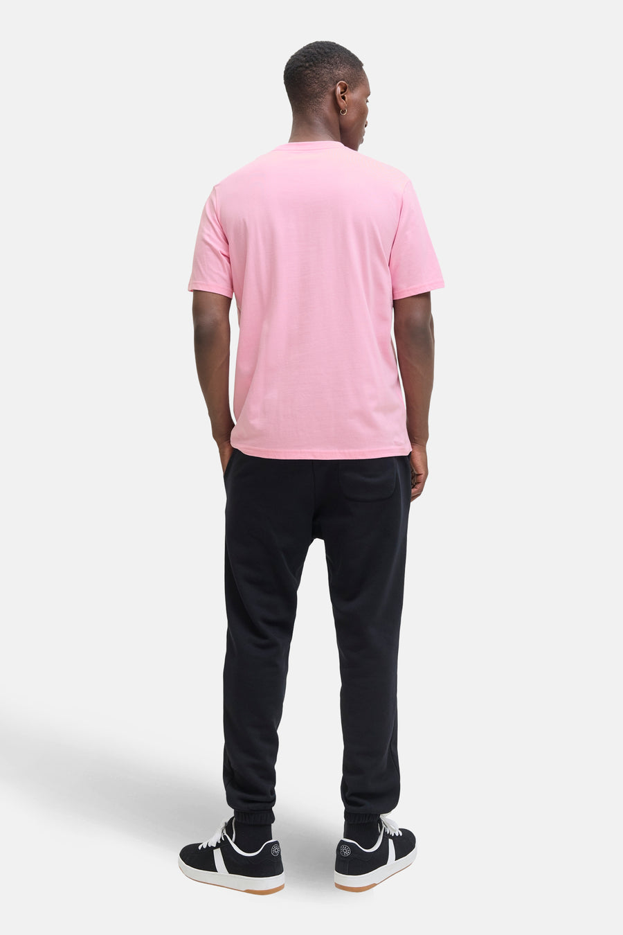 Roze T-shirt met korte mouwen van JACK & JONES, gedragen met een zwarte joggingbroek en zwart-witte sportschoenen.