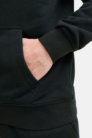Sweat à capuche noir de JACK & JONES avec une main dans la poche, en tissu texturé.