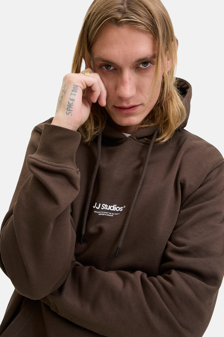 Kaki hoodie van JACK & JONES, gedragen door een blonde man met een tatoeage op zijn hand.