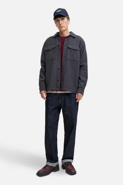 Chemise grise par PREMIUM BLUE by JACK & JONES, portée par-dessus un pull bordeaux et un jean foncé, avec une casquette.
