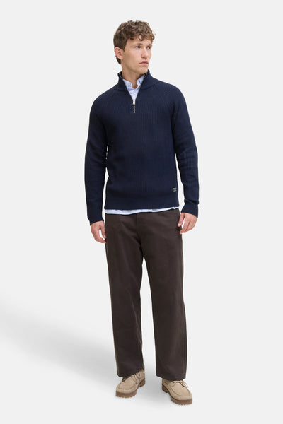 Pull col roulé bleu de JACK & JONES avec fermeture éclair argentée et détails côtelés, porté avec chemise et pantalon marron.