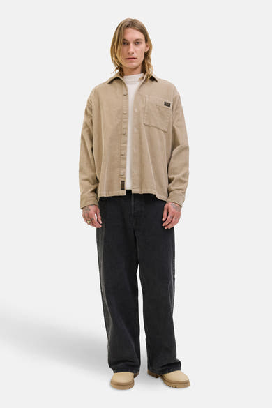 Bruine ribfluwelen overhemd met lange mouwen van PREMIUM BLUE by JACK & JONES, gedragen over een crèmekleurig T-shirt en een zwarte wijde broek.