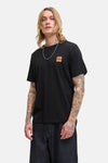 T-shirt à manches courtes noir de ORIGINALS BY JACK & JONES avec un logo carré orange sur la poitrine, porté avec un jean foncé.
