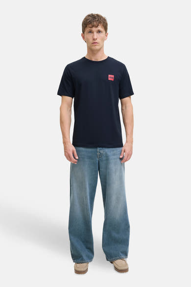 T-shirt bleu à manches courtes de ORIGINALS BY JACK & JONES avec un logo carré rouge, porté avec un jean ample bleu.