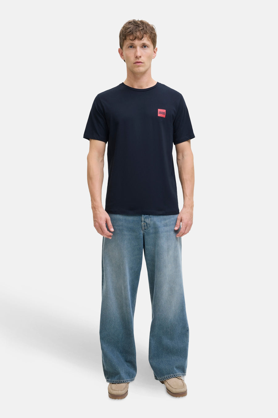 T-shirt bleu à manches courtes de ORIGINALS BY JACK & JONES avec un logo carré rouge, porté avec un jean ample bleu.