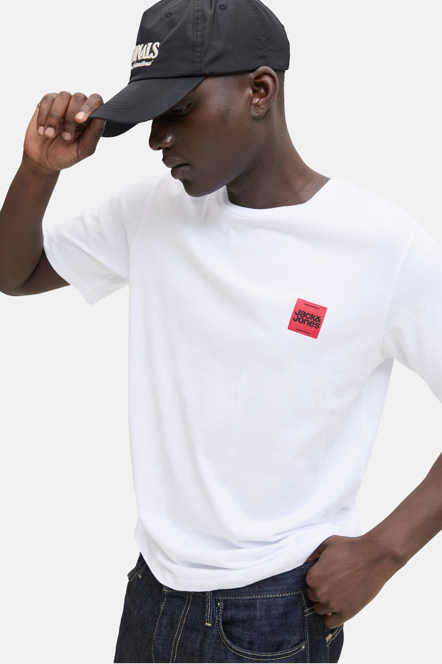 T-shirt blanc à manches courtes d'ORIGINALS BY JACK & JONES, avec un logo rouge sur la poitrine, porté avec une casquette noire.
