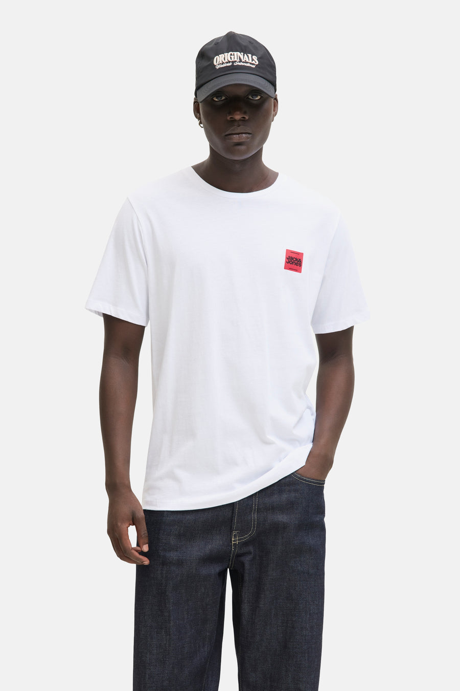 T-shirt blanc à manches courtes de ORIGINALS BY JACK & JONES, porté avec un jean brut et une casquette noire.