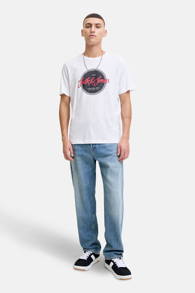 T-shirt à manches courtes blanc d'ORIGINALS BY JACK & JONES, avec un motif imprimé sur le devant, porté avec un jean bleu ample et des baskets noires.