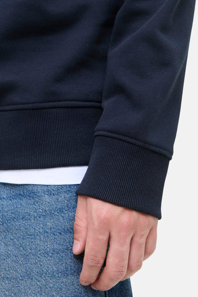 Sweat bleu de ORIGINALS BY JACK & JONES, détail du poignet côtelé sur un fond de jeans.
