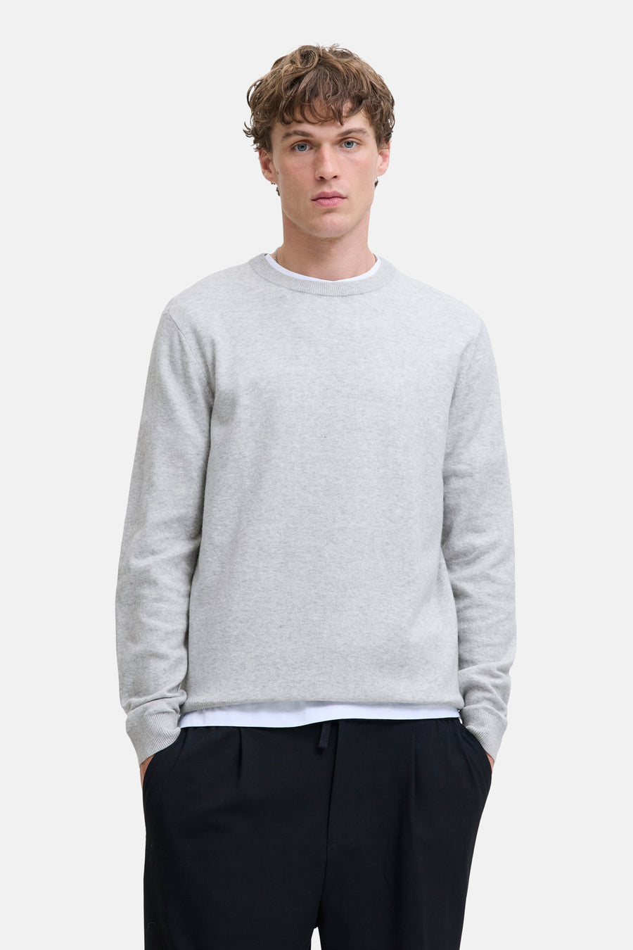 Pull à col rond gris, de PREMIUM by JACK & JONES, porté sur un t-shirt blanc, avec un pantalon noir.