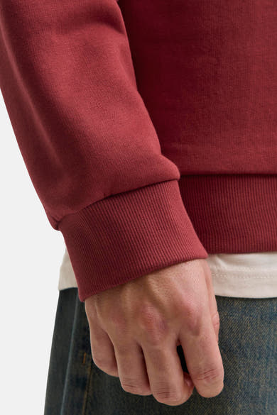 Sweat-shirt rouge de ORIGINALS BY JACK & JONES avec bordure côtelée à la manche, porté avec un t-shirt blanc et un jean.