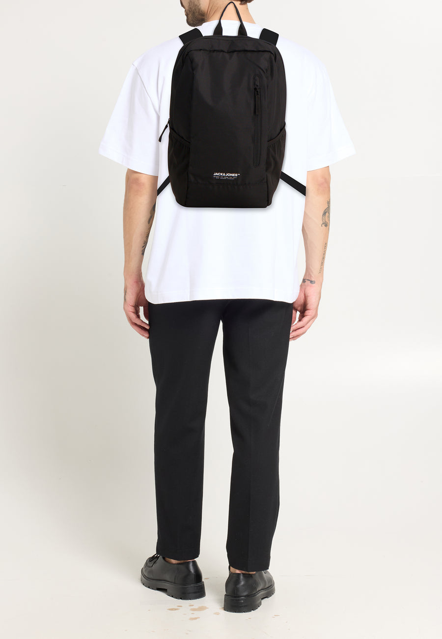 Sac à dos noir by ACCESSORIES BY JACK & JONES porté avec un t-shirt blanc et un pantalon noir.