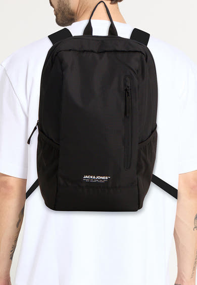 Sac à dos noir par ACCESSORIES BY JACK & JONES, avec poche zippée visible sur un homme portant un t-shirt blanc.