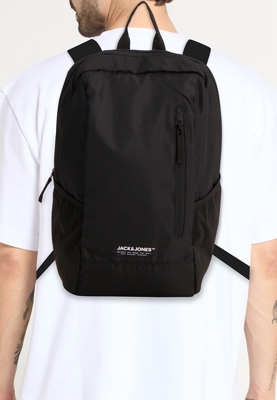 Sac à dos noir par ACCESSORIES BY JACK & JONES, avec poche zippée visible sur un homme portant un t-shirt blanc.