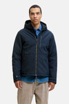 Veste courte bleue de PREMIUM BLUE by JACK & JONES portée sur une chemise en jean et un pantalon chino beige.