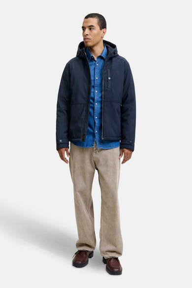 Veste courte bleue par PREMIUM BLUE by JACK & JONES, avec capuche, portée sur une chemise en jean et un pantalon beige.