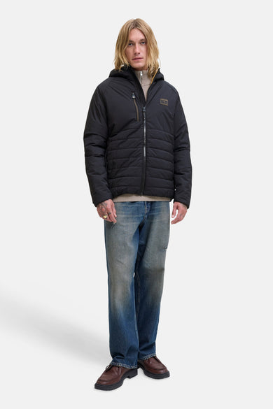 Imperméable noir par JACK & JONES, avec fermeture éclair et poches zippées, porté sur un pull beige et un jean bleu.