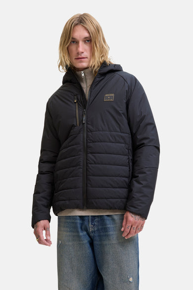 Imperméable noir de JACK & JONES, avec capuche et fermeture éclair centrale, porté avec un pull et un jean.