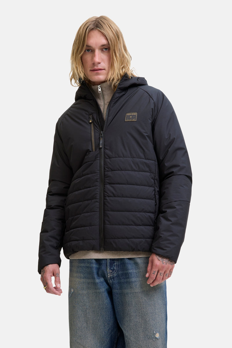 Imperméable noir de JACK & JONES, avec capuche et fermeture éclair centrale, porté avec un pull et un jean.