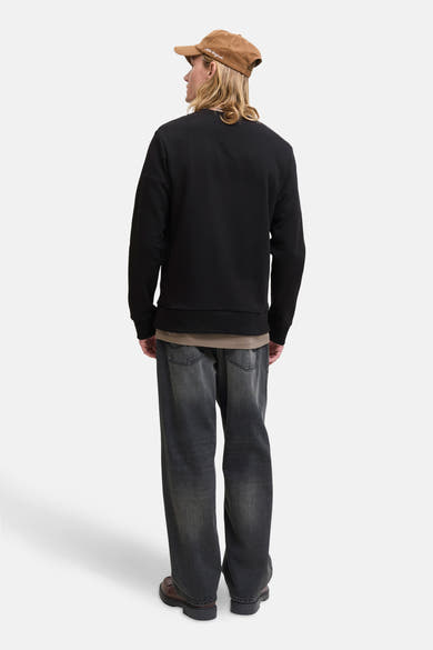 Sweat noir de ORIGINALS BY JACK & JONES, porté avec un t-shirt kaki, un jean délavé et des chaussures marron.
