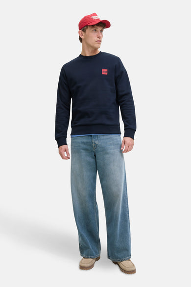 Sweat bleu col rond par ORIGINALS BY JACK & JONES, porté avec un jean ample et une casquette rouge.
