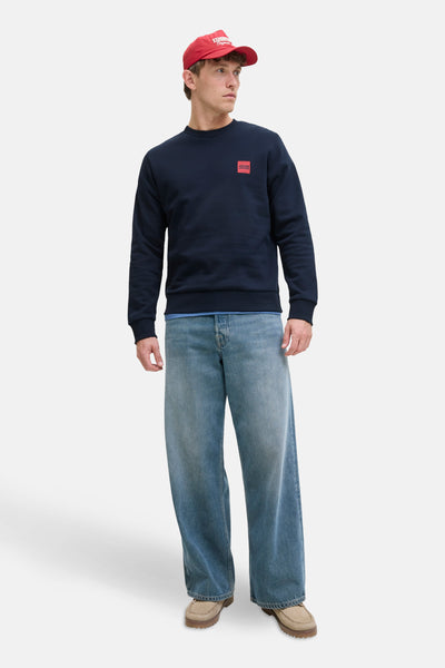 Sweat bleu col rond par ORIGINALS BY JACK & JONES, porté avec un jean ample et une casquette rouge.
