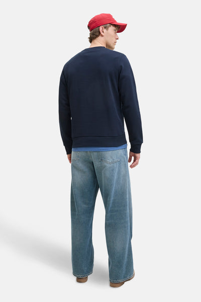 Sweat-shirt bleu marine de ORIGINALS BY JACK & JONES, porté avec un jean ample et une casquette rouge.