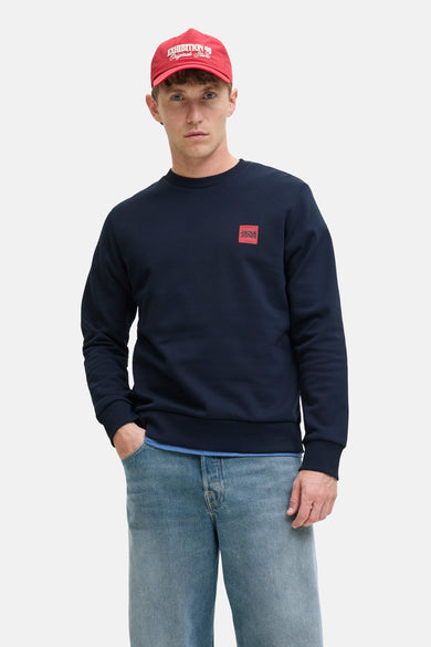 Sweat bleu marine Originals by Jack & Jones, porté avec un jean bleu clair et une casquette rouge.
