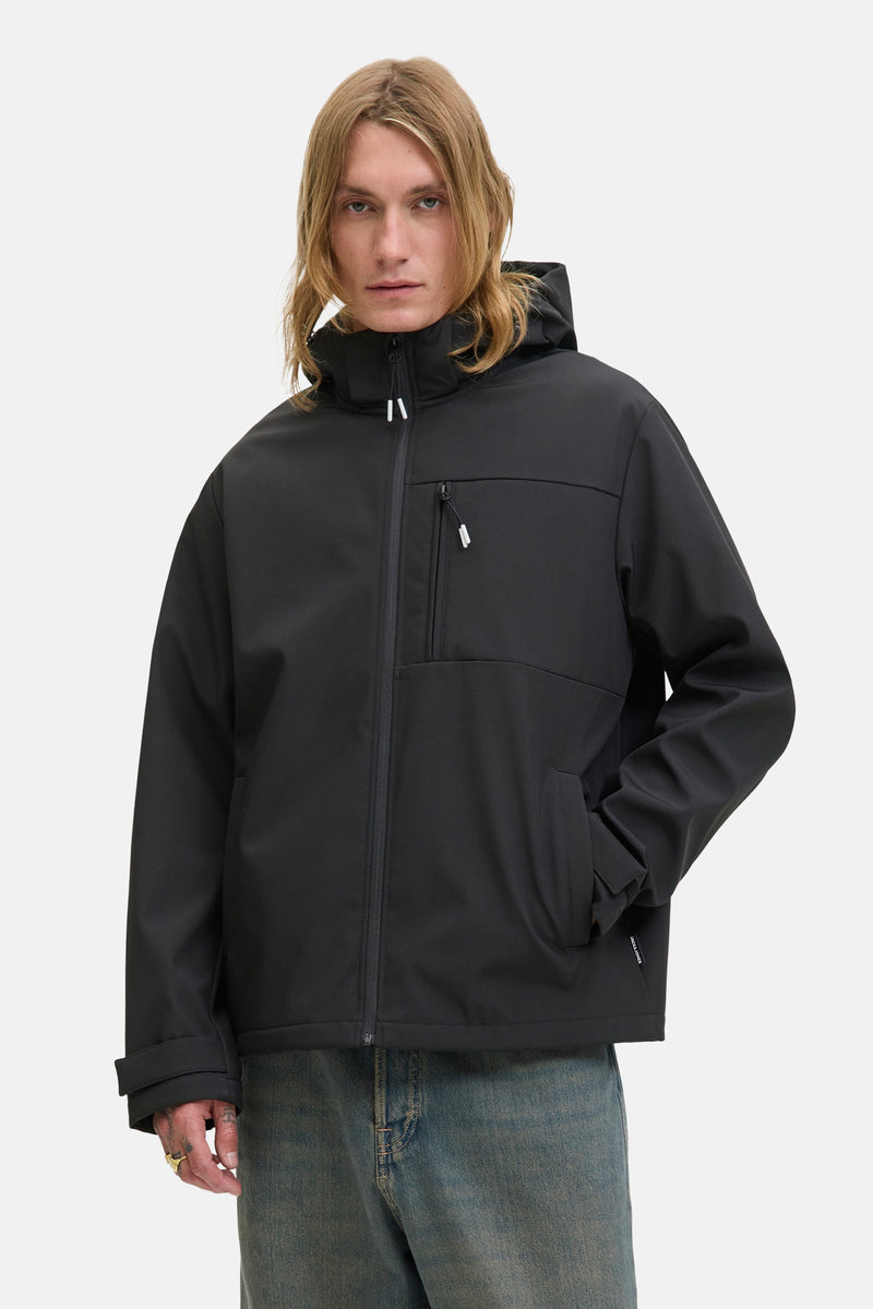 Veste courte noire par JACK & JONES avec une capuche et une fermeture éclair visible, portée avec un jean bleu.