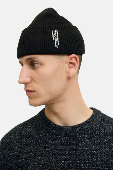 Bonnet noir par Jack & Jones, en tricot côtelé, porté avec un pull en maille mouchetée et une boucle d'oreille dorée.