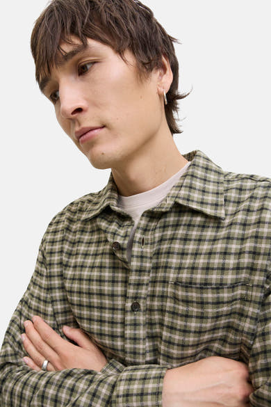 Chemise à carreaux vert et noir de JACK & JONES, portée sur un t-shirt, avec une boucle d'oreille et une bague.

